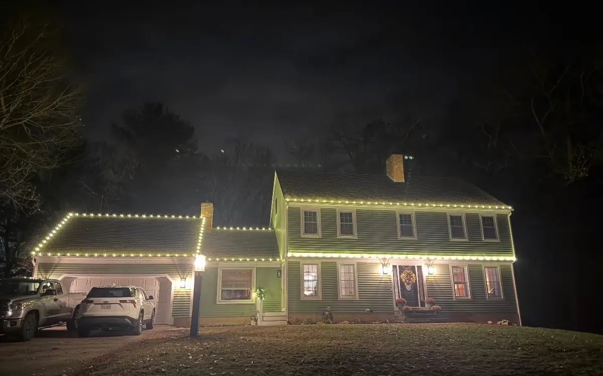 A two-story home photographed from the street with warm white lights running the full length of the roofline.