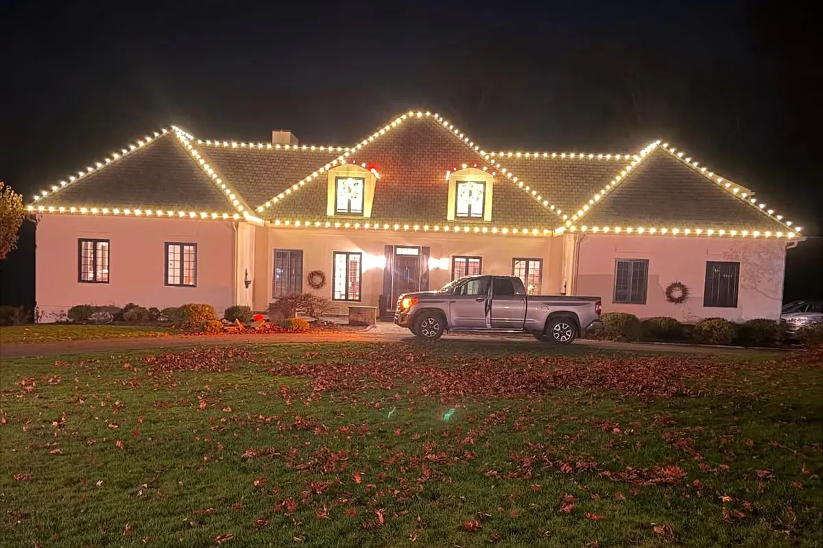 A wide single-story home with warm white lights following every gable peak, seen across a deep front lawn.